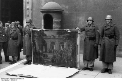 Soldati schierati a Piazza Venezia mentre mostrano un grande dipinto durante la cerimonia di restituzione delle opere d’arte.