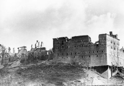 Veduta in bianco e nero dell’abbazia di Montecassino gravemente danneggiata dai bombardamenti della Seconda Guerra Mondiale, con muri crollati, finestre distrutte e vaste porzioni dell’edificio ridotte a macerie sulla collina.